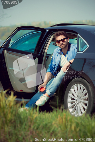 Image of Handsome smiling man sitting in his car with opened doors