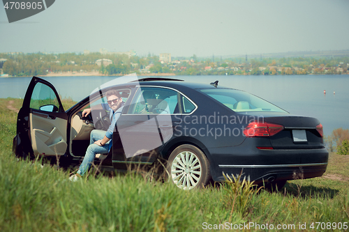 Image of Handsome smiling man sitting in his car with opened doors