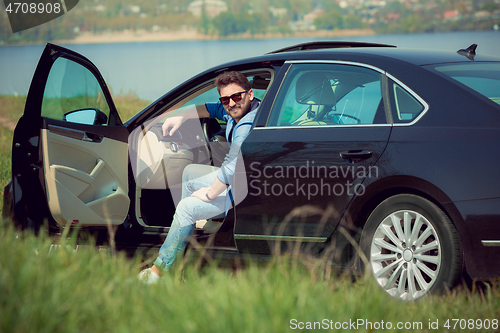 Image of Handsome smiling man sitting in his car with opened doors