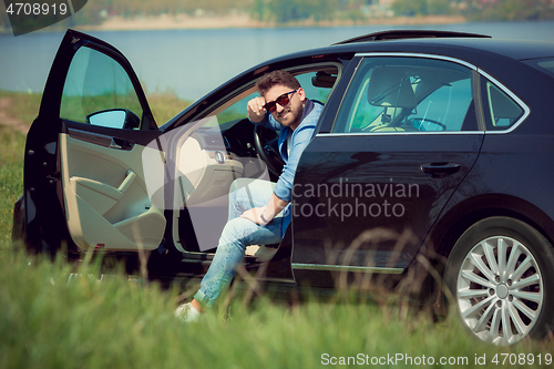 Image of Handsome smiling man sitting in his car with opened doors