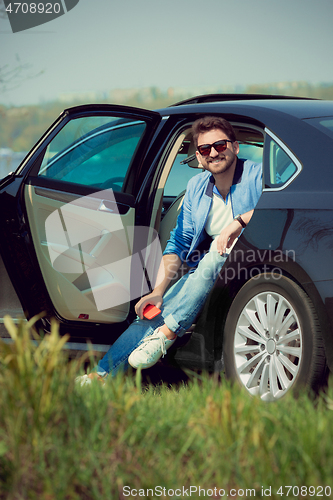 Image of Handsome smiling man sitting in his car with opened doors