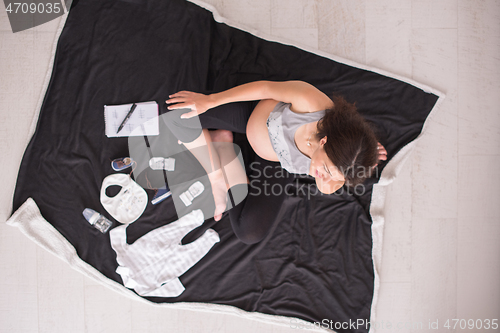 Image of top view of pregnant woman checking list of baby clothes