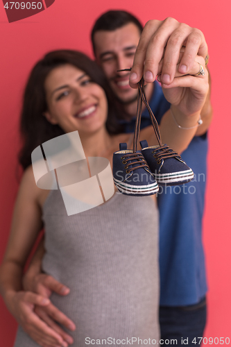 Image of young pregnant couple holding newborn baby shoes