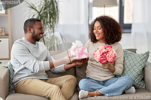 Image of happy couple with flowers and gift at home