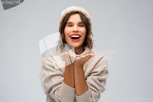 Image of young woman in knitted winter hat sending air kiss