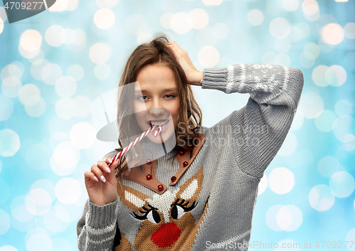 Image of woman in christmas sweater biting candy cane