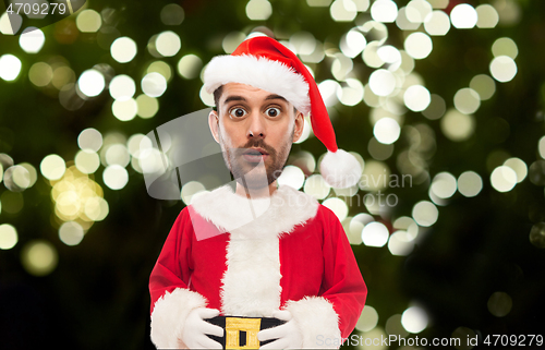 Image of surprised man in santa costume over christmas tree