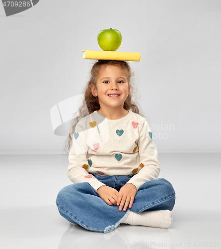 Image of little girl with book and apple sitting on floor