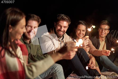 Image of happy friends with sparklers on beach at night