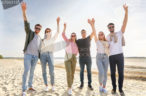 Image of happy friends waving hands on beach in summer