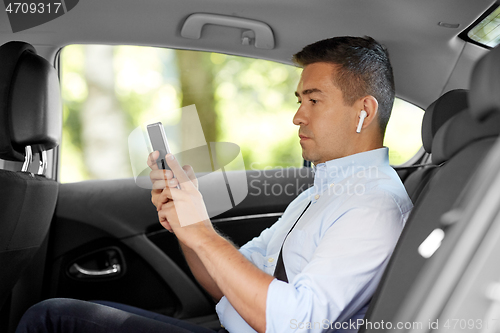 Image of passenger with earphones and cellphone in taxi car