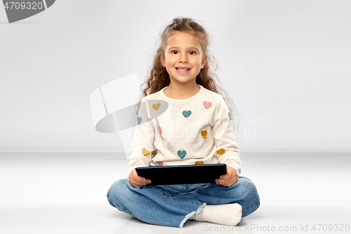 Image of smiling girl with tablet computer sitting on floor