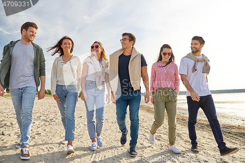 Image of happy friends walking along summer beach