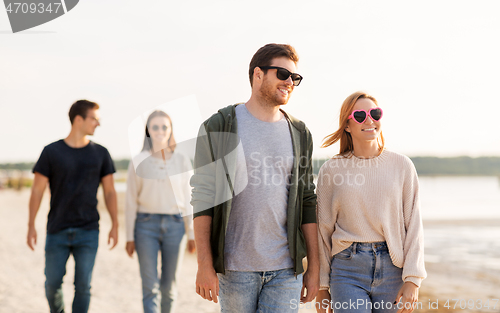 Image of happy friends walking along summer beach