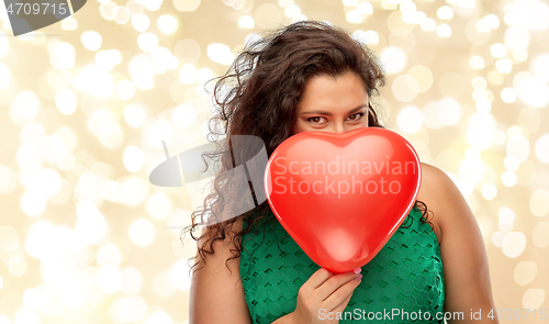 Image of playful woman holding red heart shaped balloon