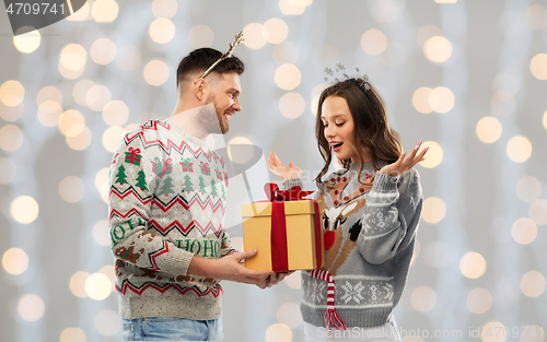 Image of happy couple in ugly sweaters with christmas gift