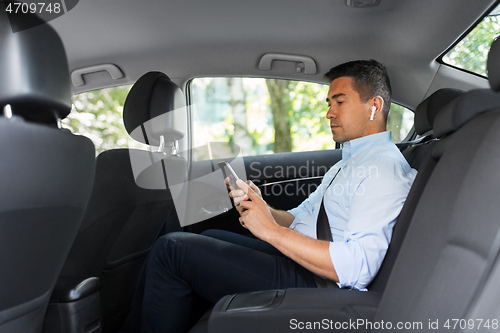 Image of passenger with earphones and cellphone in taxi car