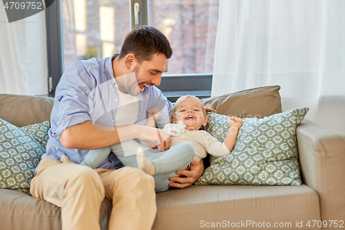 Image of happy father tickling little baby daughter at home