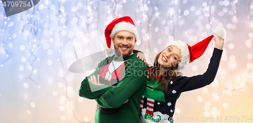 Image of happy couple in christmas sweaters and santa hats