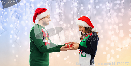 Image of happy couple in christmas sweaters with gift box