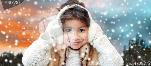 Image of happy little girl in earmuffs over winter forest