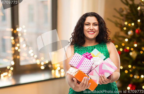 Image of happy woman holding gifts over christmas tree