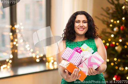 Image of happy woman holding gifts over christmas tree