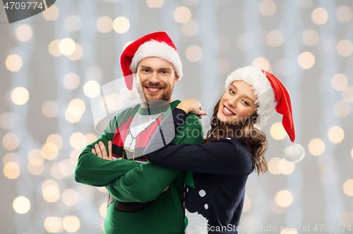 Image of happy couple in christmas sweaters and santa hats