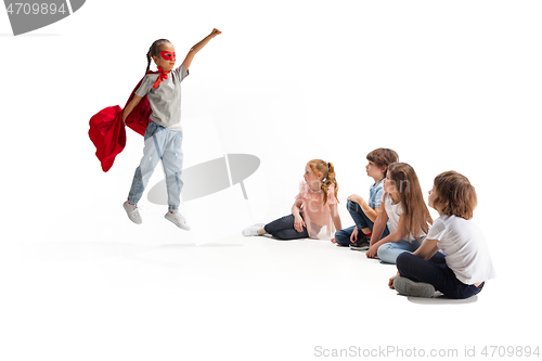 Image of Child pretending to be a superhero with her friends sitting around