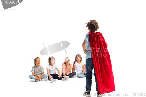 Image of Child pretending to be a superhero with his friends sitting around