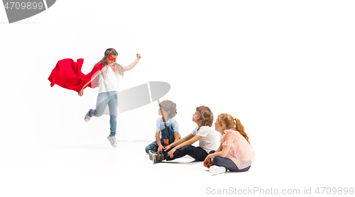 Image of Child pretending to be a superhero with her friends sitting around