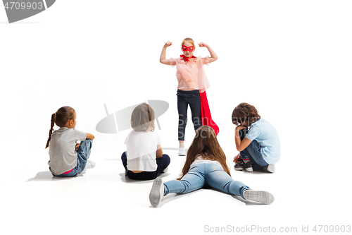 Image of Child pretending to be a superhero with her friends sitting around