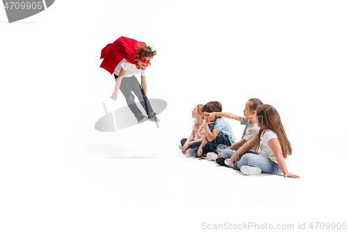 Image of Child pretending to be a superhero with his friends sitting around