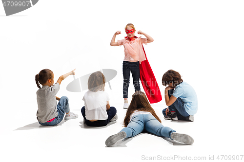 Image of Child pretending to be a superhero with her friends sitting around