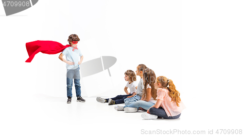 Image of Child pretending to be a superhero with his friends sitting around