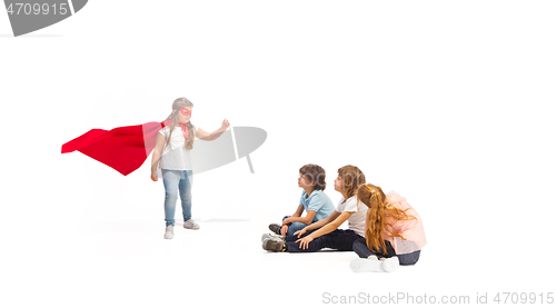 Image of Child pretending to be a superhero with her friends sitting around