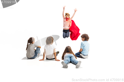 Image of Child pretending to be a superhero with her friends sitting around