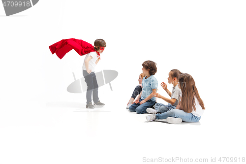 Image of Child pretending to be a superhero with his friends sitting around