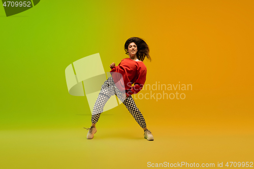 Image of Stylish sportive girl dancing hip-hop in stylish clothes on colorful background at dance hall in neon light. Youth culture, movement, style and fashion, action.