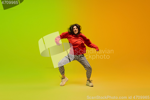 Image of Stylish sportive girl dancing hip-hop in stylish clothes on colorful background at dance hall in neon light. Youth culture, movement, style and fashion, action.