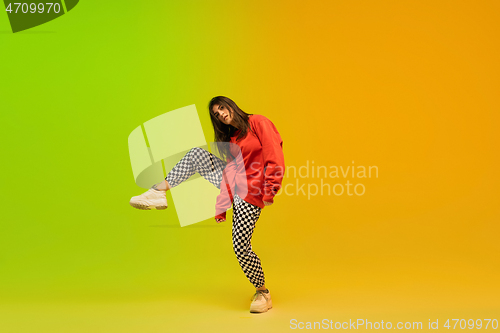 Image of Stylish sportive girl dancing hip-hop in stylish clothes on colorful background at dance hall in neon light. Youth culture, movement, style and fashion, action.