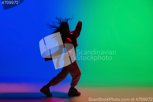 Image of Stylish sportive girl dancing hip-hop in stylish clothes on colorful background at dance hall in neon light. Youth culture, movement, style and fashion, action.