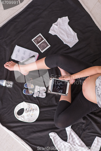 Image of top view of pregnant woman checking list of baby clothes