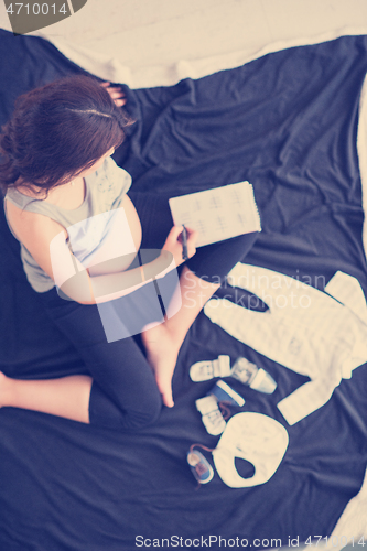 Image of top view of pregnant woman checking list of baby clothes