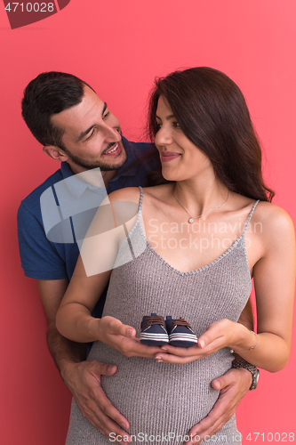 Image of young pregnant couple holding newborn baby shoes