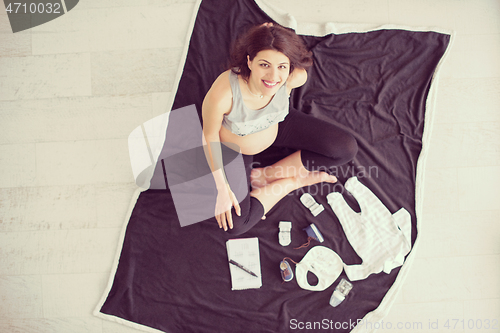 Image of top view of pregnant woman checking list of baby clothes