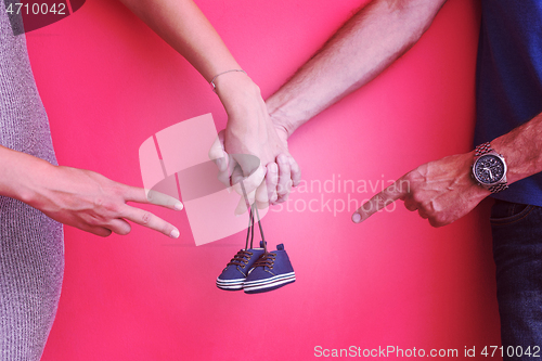 Image of young pregnant couple holding newborn baby shoes