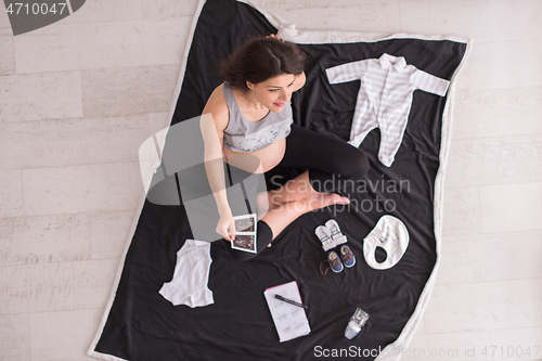 Image of top view of pregnant woman checking list of baby clothes