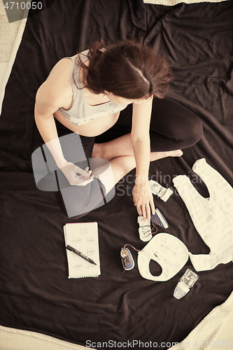 Image of top view of pregnant woman checking list of baby clothes