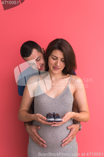 Image of young pregnant couple holding newborn baby shoes